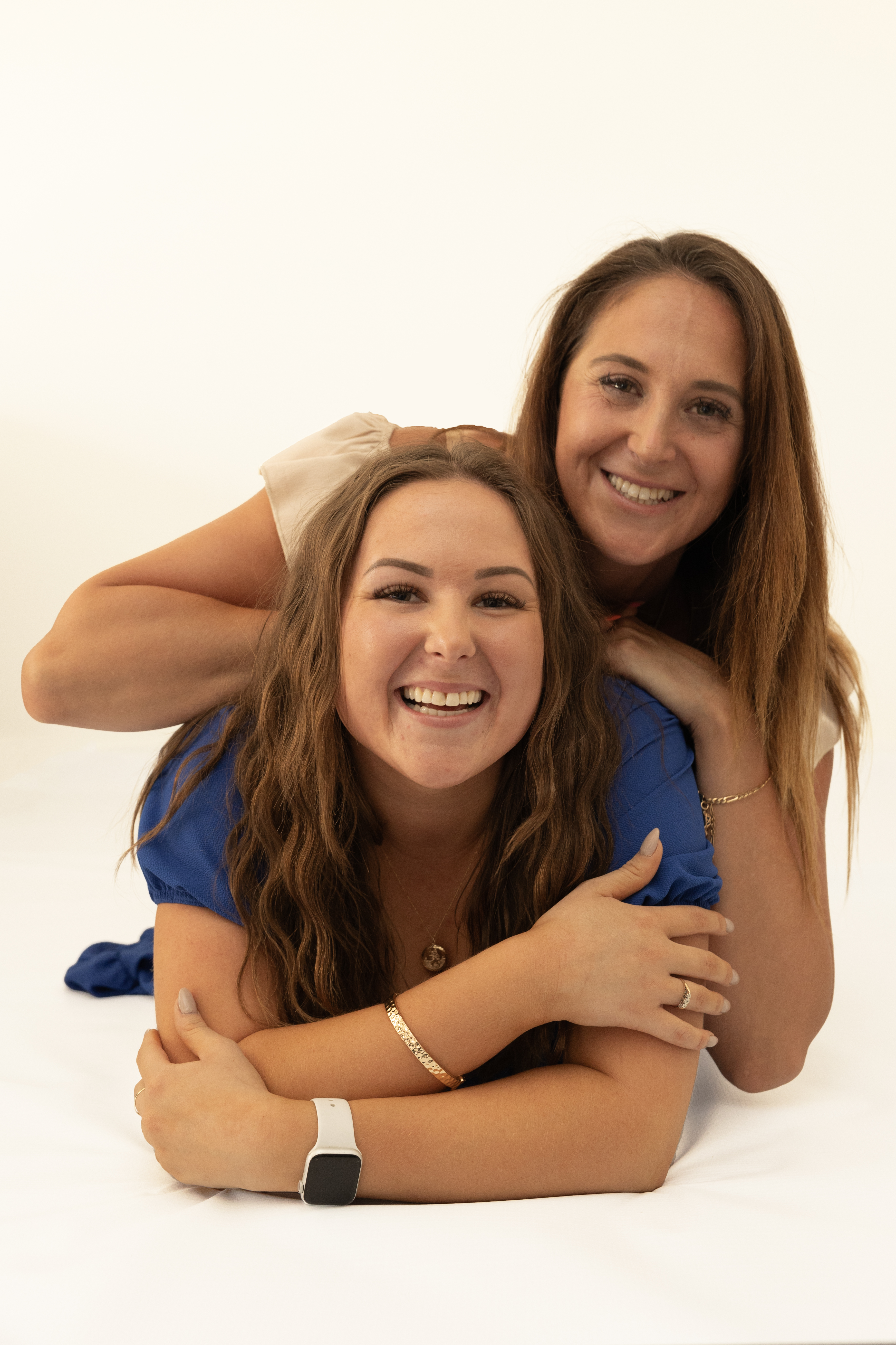Sisters smiling together during a relaxed white background studio portrait session.