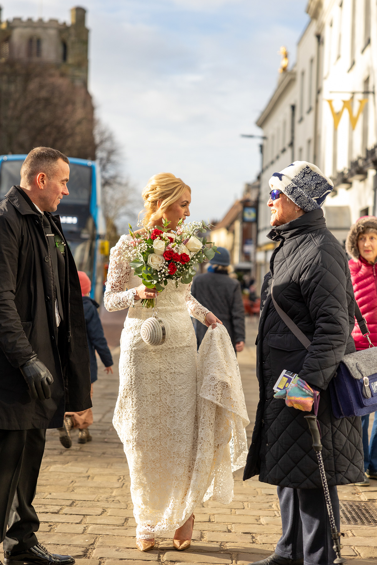 Bride and groom speaking with a passer-by in a town centre shortly after their wedding ceremony.