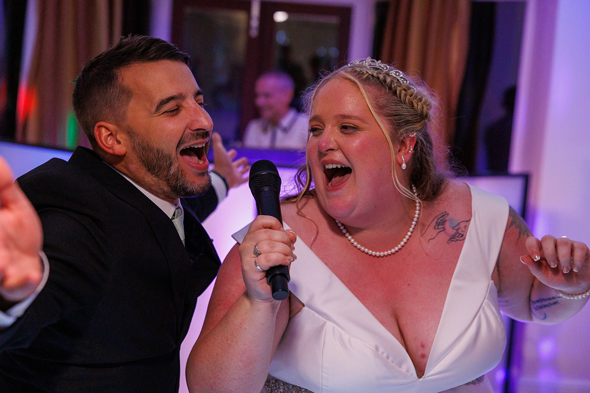 Bride and groom singing into a microphone together during a lively evening wedding reception.