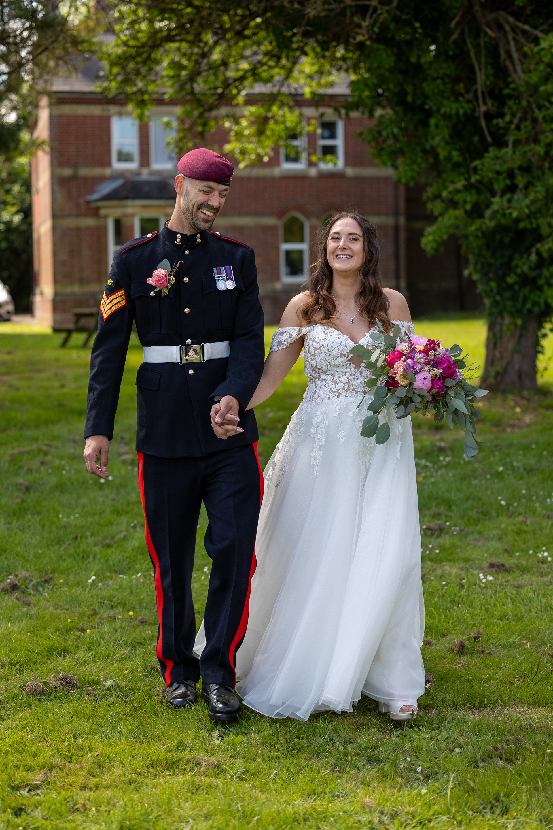 Bride and groom holding hands and walking through gardens after their wedding ceremony, with the groom wearing formal military uniform.