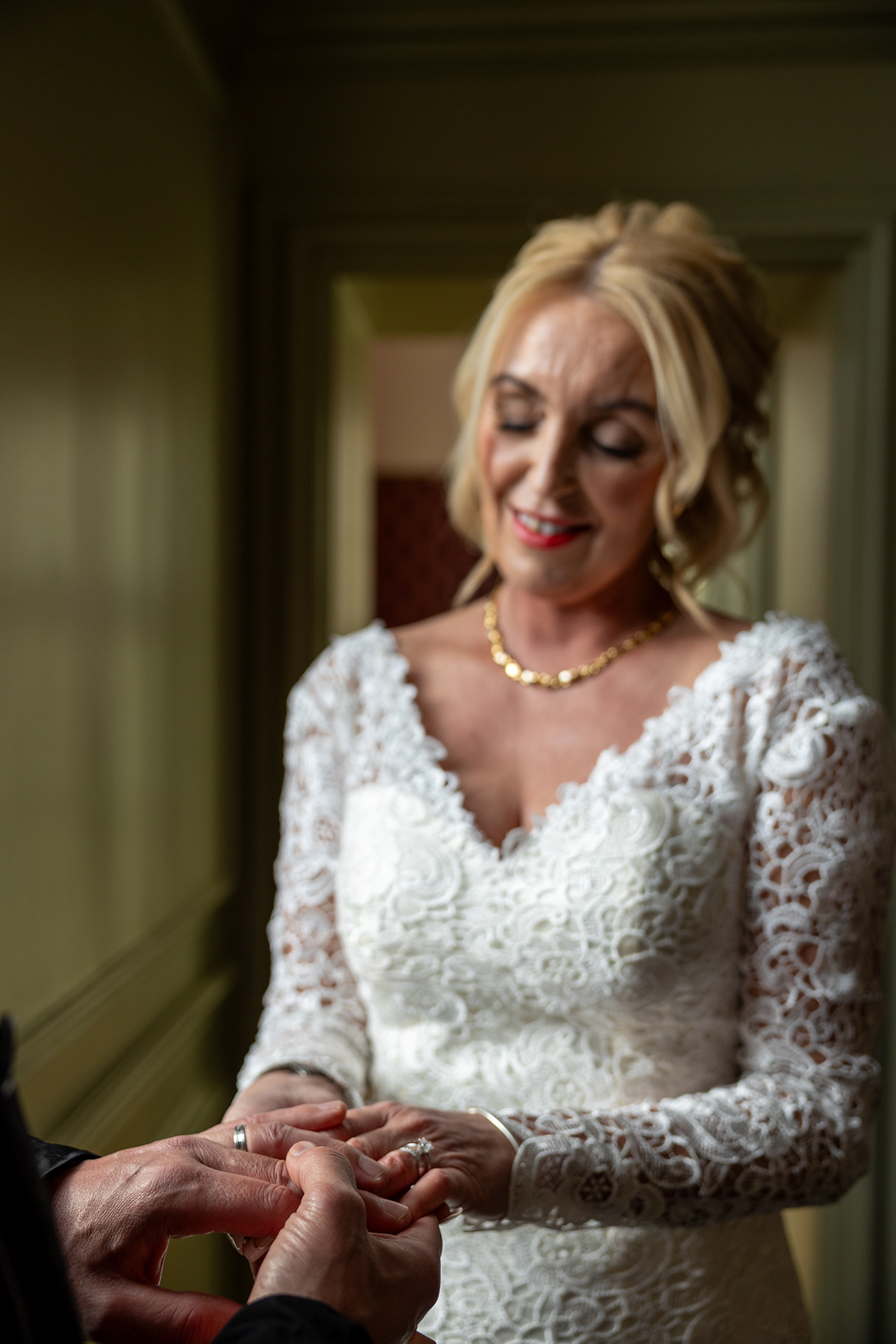 Close-up photograph of a bride smiling as a wedding ring is placed onto her finger during the ceremony.