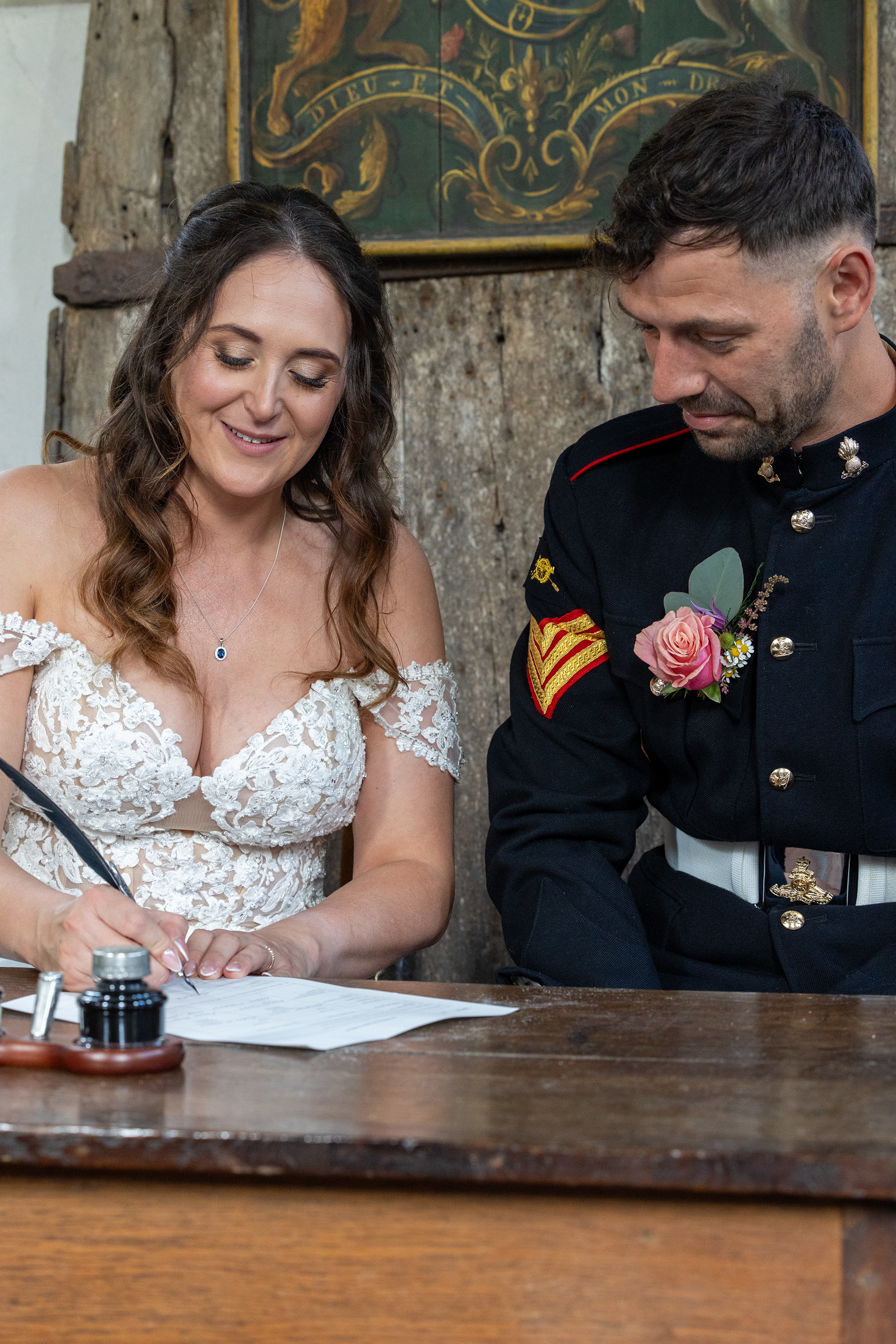 Bride signing the wedding register while seated beside the groom in formal military uniform during the ceremony.