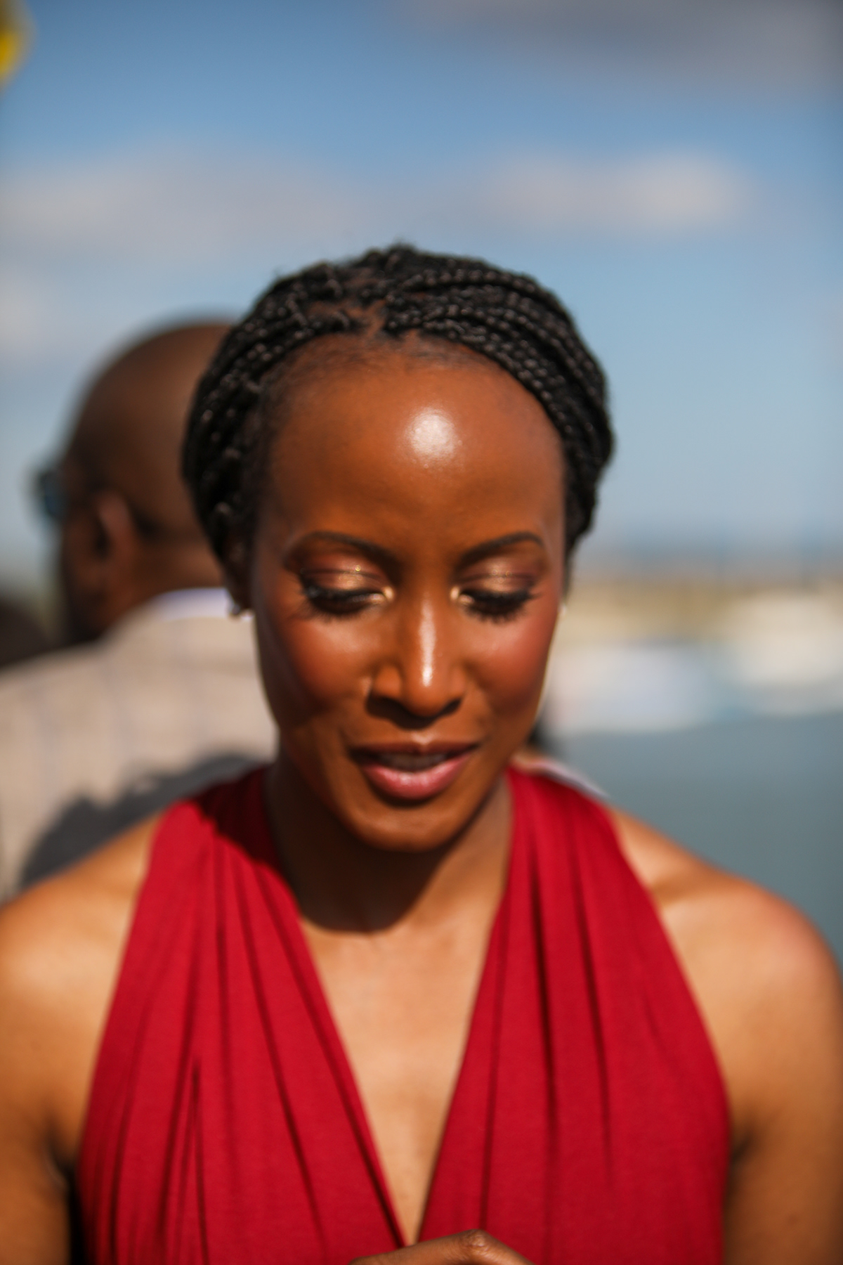 Close portrait of a wedding guest in a red dress outdoors beside the water in warm evening sunlight.
