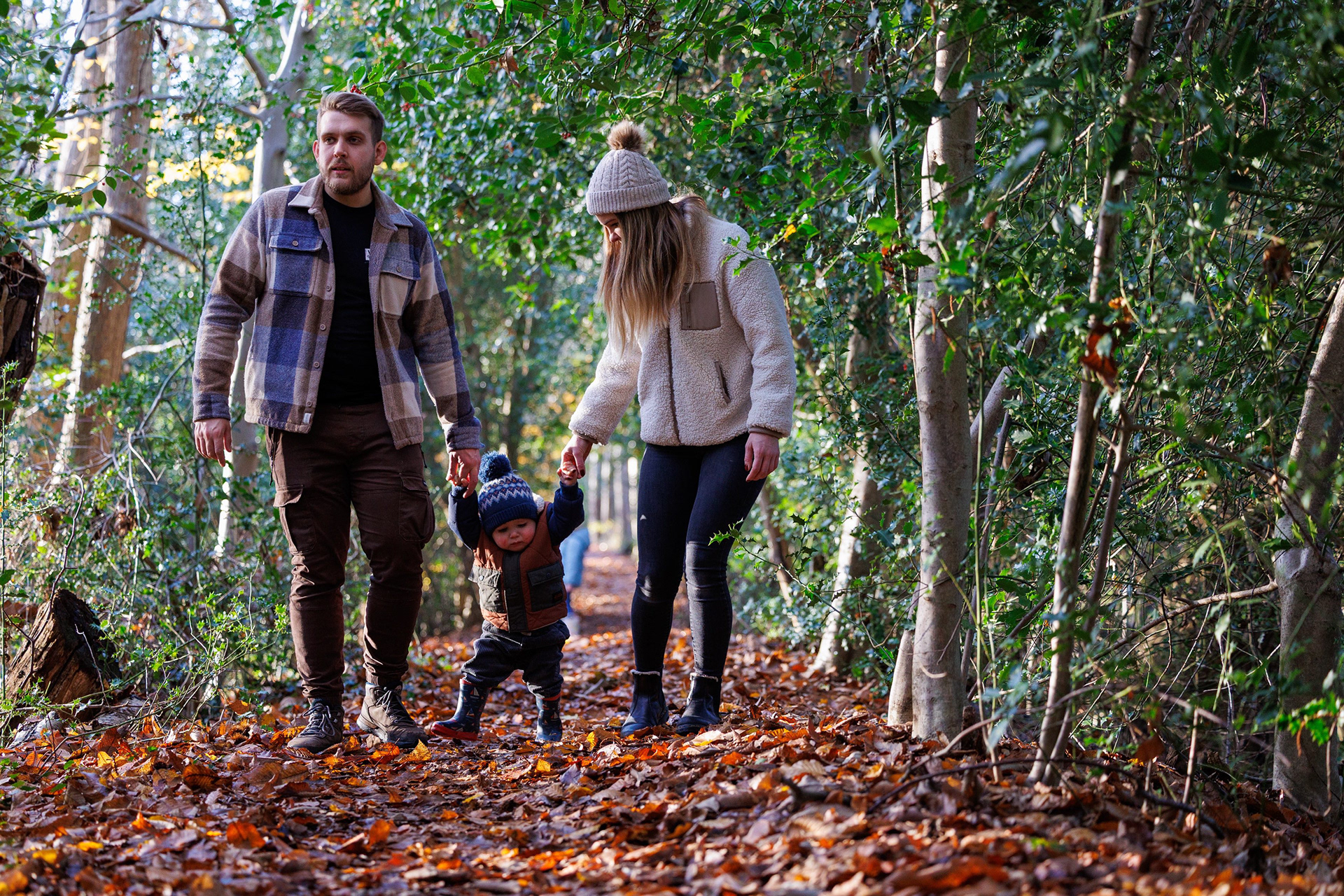 Young family walking through woodland with their toddler during an autumn outdoor portrait session.