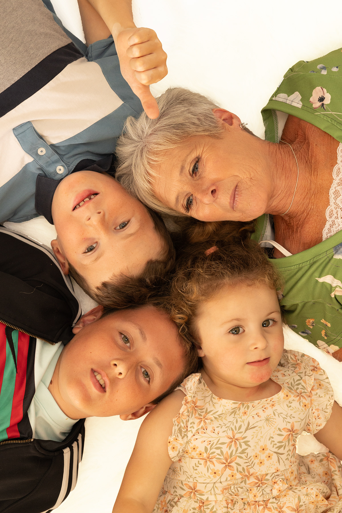 Overhead family portrait featuring a grandmother and three children lying together and smiling at the camera.