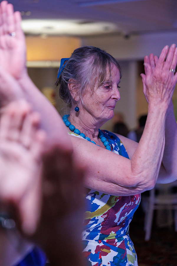 Wedding guest dancing with raised hands during an evening reception under colourful party lighting.