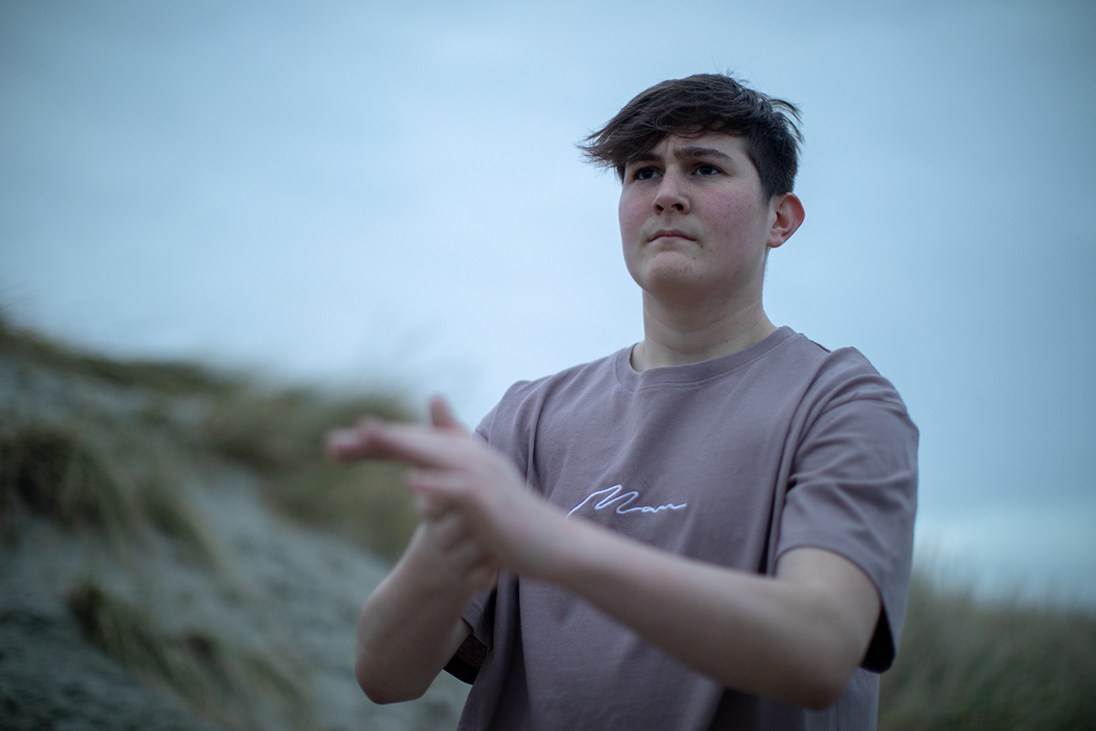 Teenage boy standing outdoors near sand dunes during an atmospheric coastal portrait session.