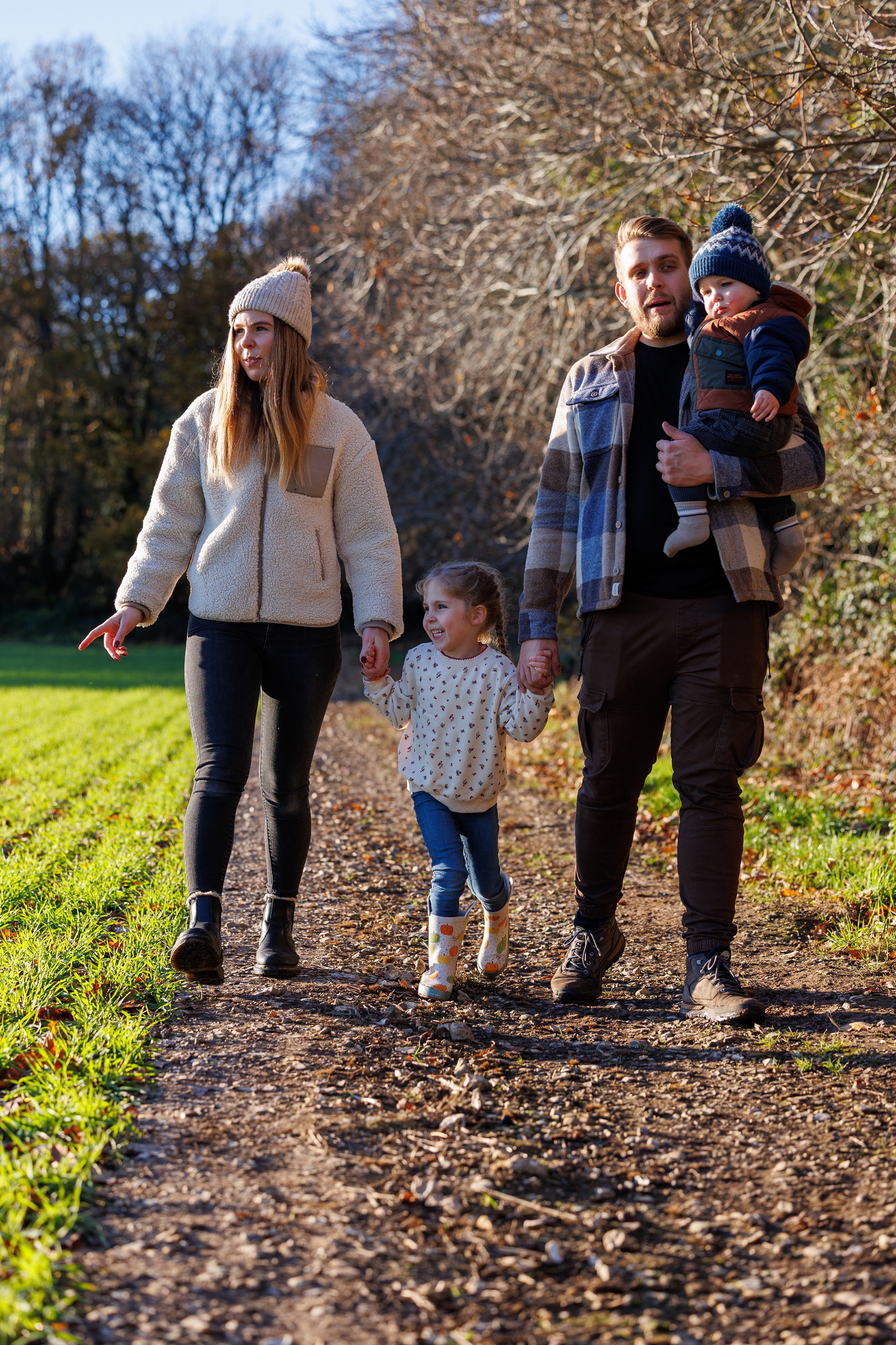 Family walking together along a countryside path during an autumn outdoor portrait session.