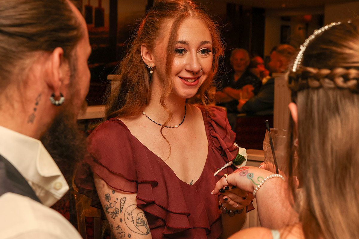 Candid photograph of wedding guests talking and smiling together during a warmly lit evening reception indoors.