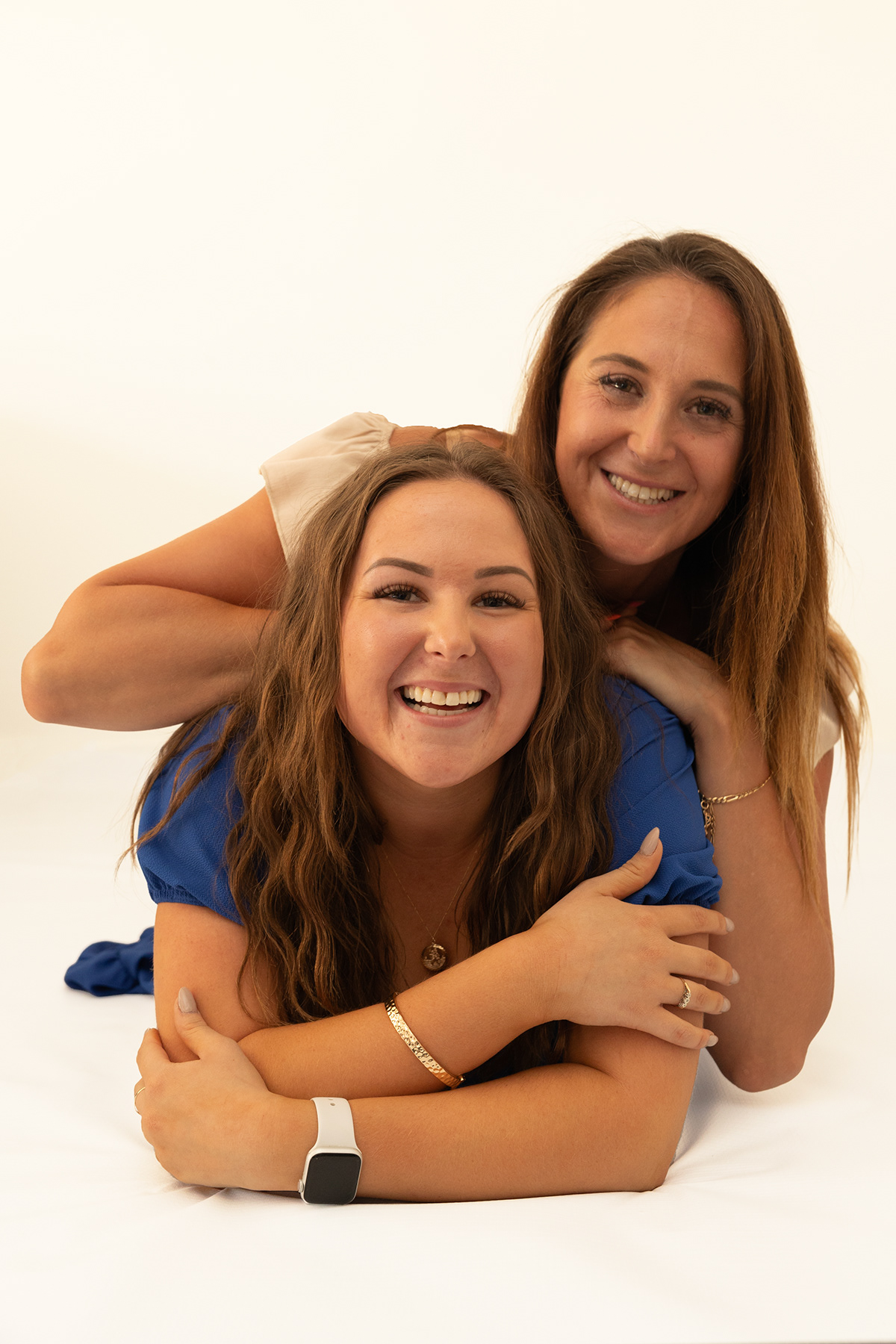 Sisters smiling together during a relaxed white background studio portrait session.