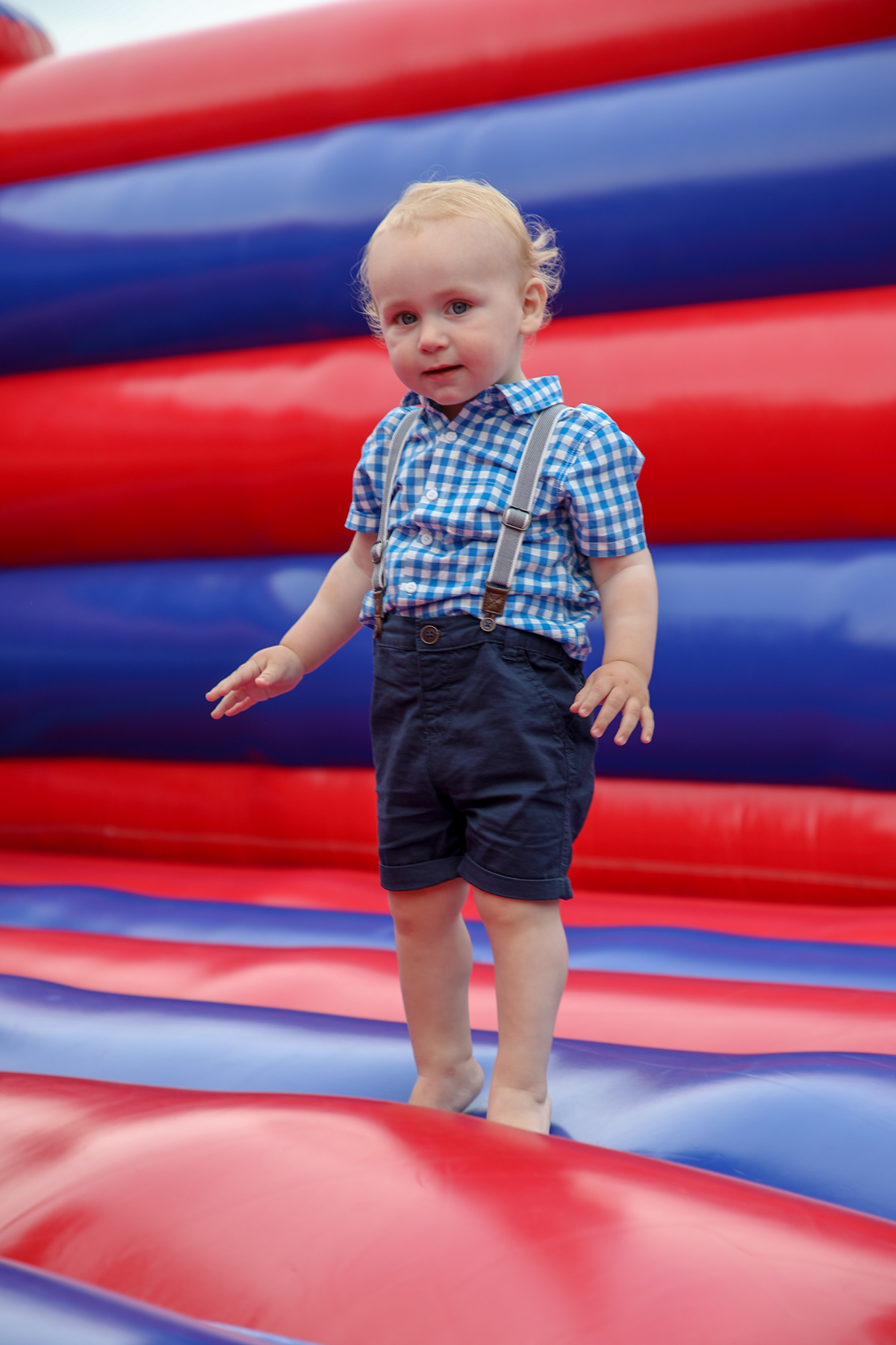 Toddler standing on a red and blue inflatable bouncy castle during a children’s party or outdoor family event.
