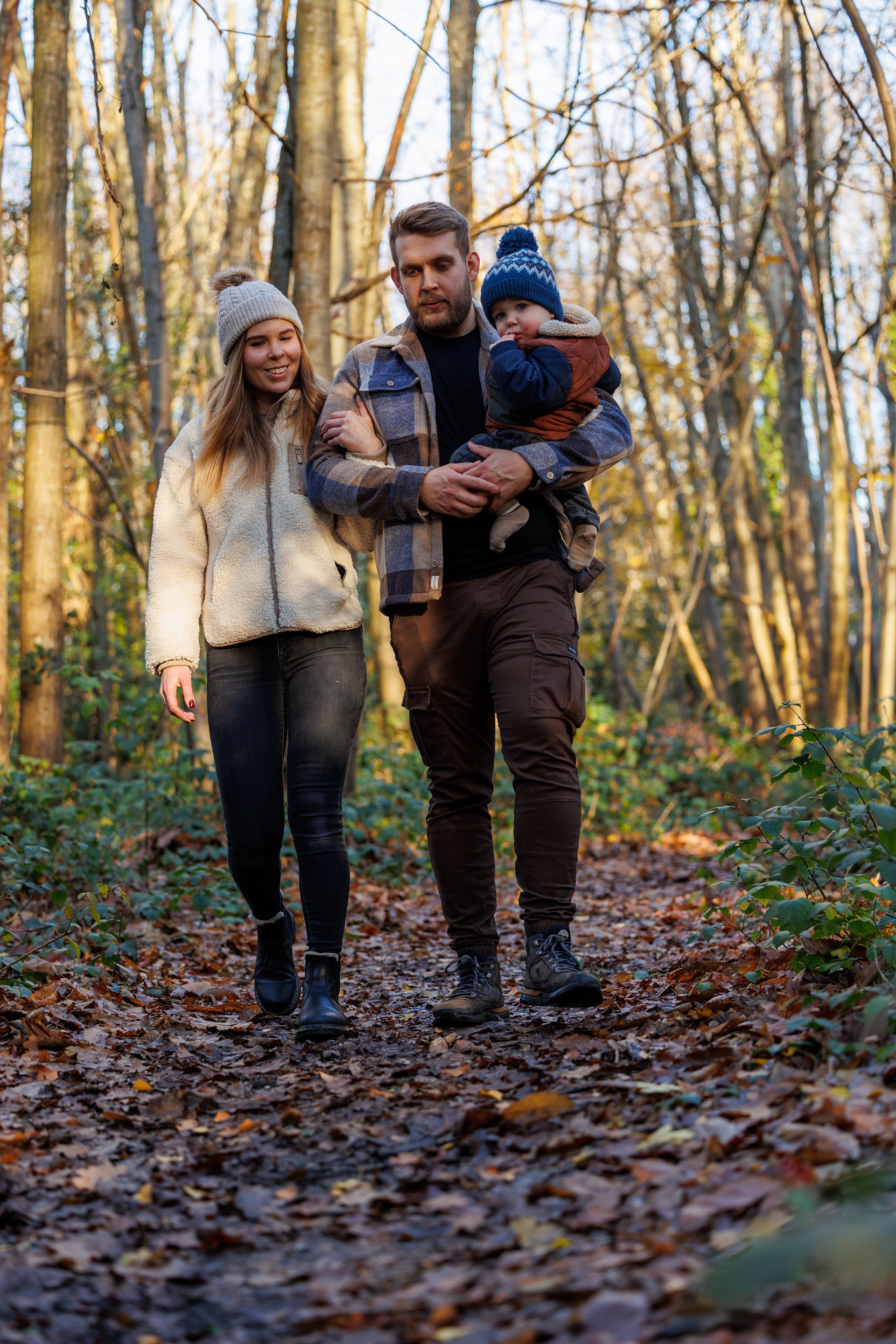 Parents walking through woodland with their young child during a relaxed outdoor family portrait session.